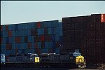 Shipping containers piled high in depots near ports in the U.S.A. illustrate America's trade deficit. Near Port Newark, New Jersey, container depots use special equipment to stack containers up to eight (8) high. Trucks drop off empty containers for storage or pick up empty ones for use. Depots resemble cities or monuments, blocking the skylines of Newark, N.J., and New York City.