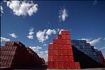 Shipping containers piled high in depots near ports in the U.S.A. illustrate America's trade deficit. Near Port Newark, New Jersey, container depots use special equipment to stack containers up to eight (8) high. Trucks drop off empty containers for storage or pick up empty ones for use. Depots resemble cities or monuments, blocking the skylines of Newark, N.J., and New York City.