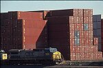 Shipping containers piled high in depots near ports in the U.S.A. illustrate America's trade deficit. Near Port Newark, New Jersey, container depots use special equipment to stack containers up to eight (8) high. Trucks drop off empty containers for storage or pick up empty ones for use. Depots resemble cities or monuments, blocking the skylines of Newark, N.J., and New York City.