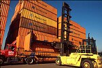 Shipping containers piled high in depots near ports in the U.S.A. illustrate America's trade deficit. Near Port Newark, New Jersey, container depots use special equipment to stack containers up to eight (8) high. Trucks drop off empty containers for storage or pick up empty ones for use. Depots resemble cities or monuments, blocking the skylines of Newark, N.J., and New York City.