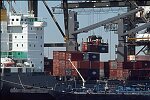 Shipping containers piled high in depots near ports in the U.S.A. illustrate America's trade deficit. Near Port Newark, New Jersey, container depots use special equipment to stack containers up to eight (8) high. Trucks drop off empty containers for storage or pick up empty ones for use. Depots resemble cities or monuments, blocking the skylines of Newark, N.J., and New York City.