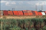 Shipping containers piled high in depots near ports in the U.S.A. illustrate America's trade deficit. Near Port Newark, New Jersey, container depots use special equipment to stack containers up to eight (8) high. Trucks drop off empty containers for storage or pick up empty ones for use. Depots resemble cities or monuments, blocking the skylines of Newark, N.J., and New York City.