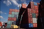 Shipping containers piled high in depots near ports in the U.S.A. illustrate America's trade deficit. Near Port Newark, New Jersey, container depots use special equipment to stack containers up to eight (8) high. Trucks drop off empty containers for storage or pick up empty ones for use. Depots resemble cities or monuments, blocking the skylines of Newark, N.J., and New York City.