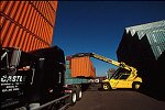 Shipping containers piled high in depots near ports in the U.S.A. illustrate America's trade deficit. Near Port Newark, New Jersey, container depots use special equipment to stack containers up to eight (8) high. Trucks drop off empty containers for storage or pick up empty ones for use. Depots resemble cities or monuments, blocking the skylines of Newark, N.J., and New York City.