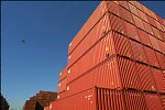 Shipping containers piled high in depots near ports in the U.S.A. illustrate America's trade deficit. Near Port Newark, New Jersey, container depots use special equipment to stack containers up to eight (8) high. Trucks drop off empty containers for storage or pick up empty ones for use. Depots resemble cities or monuments, blocking the skylines of Newark, N.J., and New York City.