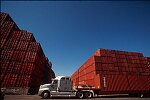 Shipping containers piled high in depots near ports in the U.S.A. illustrate America's trade deficit. Near Port Newark, New Jersey, container depots use special equipment to stack containers up to eight (8) high. Trucks drop off empty containers for storage or pick up empty ones for use. Depots resemble cities or monuments, blocking the skylines of Newark, N.J., and New York City.